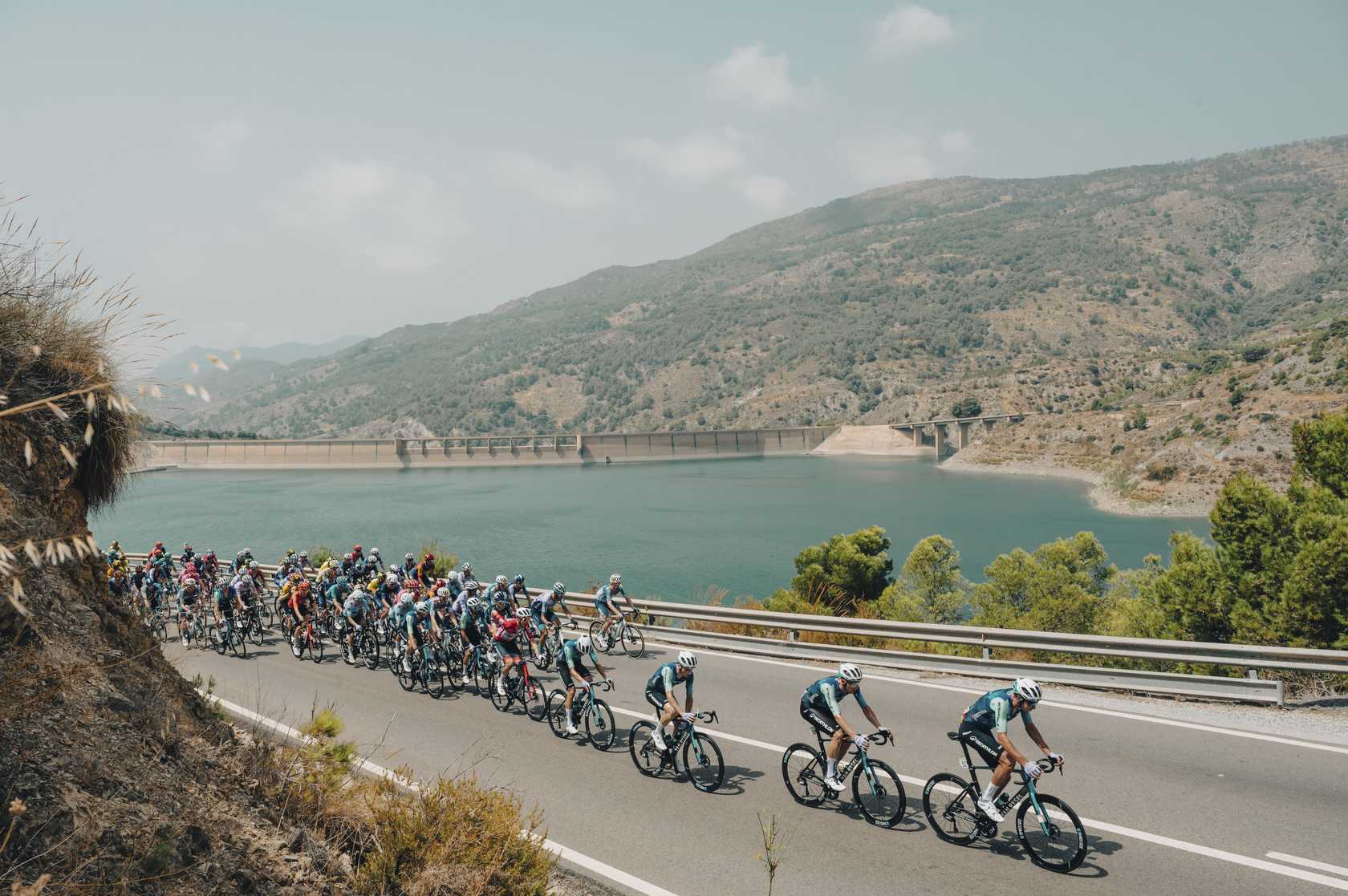 El pelotón pasa junto al Embalse de Canales durante la última etapa de La Vuelta con meta en Granada disputada hasta la fecha, en 2024. Foto: Unipublic / Cxcling